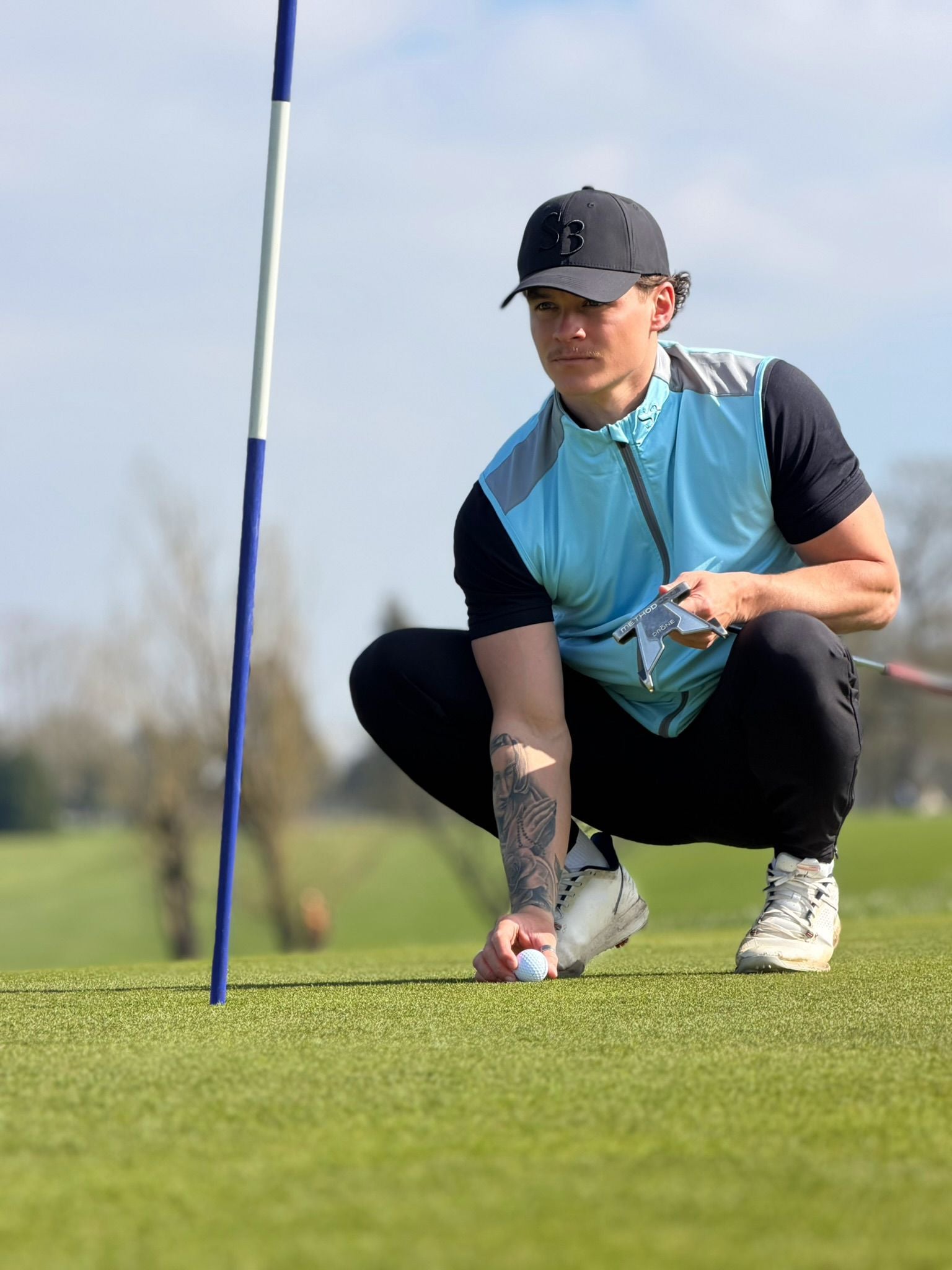 S3 golfer crouched on the green placing a ball, open sky behind