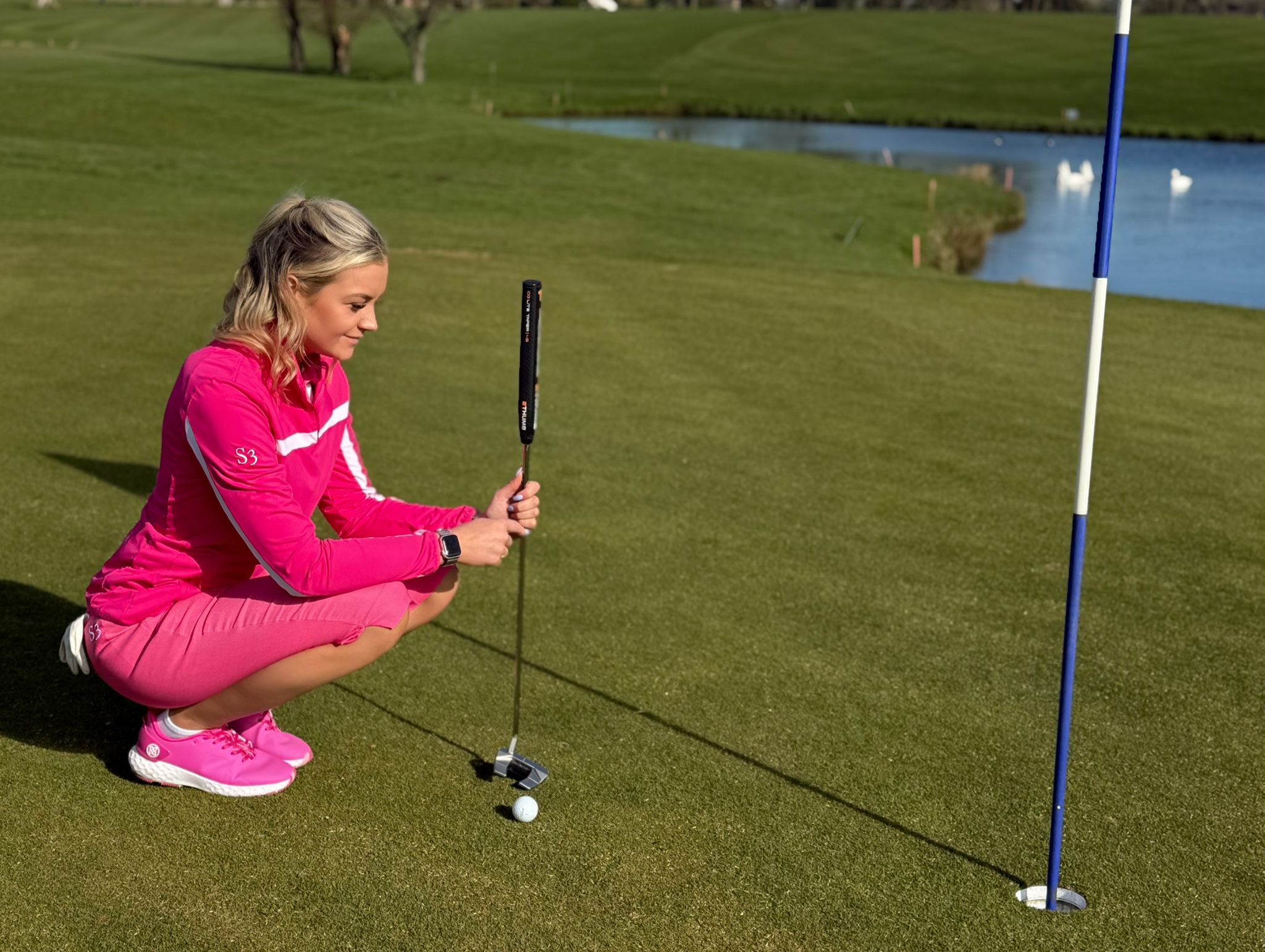 S3 golfer in pink lining up a putt beside the water